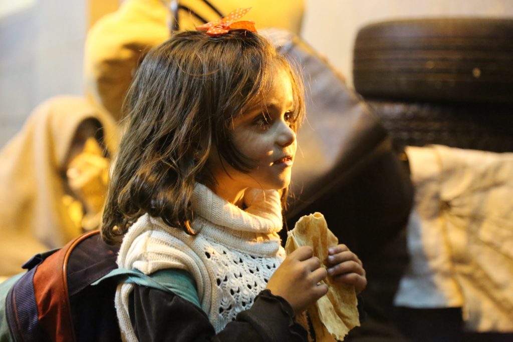 On 11 January 2016 in Madaya, Rural Damascus, a girl eats bread, as she and other children and their families wait for permissions to leave the besieged town. “Children were waiting for us for a long time but few remained on the streets when the convoy made it inside Madaya after dark,” added Ismail. “The few children who did stay out to receive the convoys were cold and stormed to the team to ask for biscuits or bread or anything that they could eat immediately.” (UNICEF/UN07224/Al Saleh, WFP) 